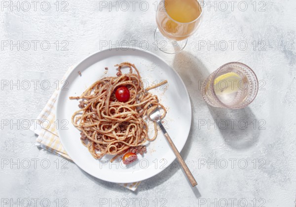 A plate with spaghetti topped with tomato sauce and cherry tomatoes sits on a light table. A glass of cool drink accompanies the meal, creating a relaxed dining atmosphere