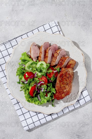 Grilled duck breast is beautifully presented beside a colorful salad of greens, cucumbers, tomatoes, and red onions, highlighting a well-prepared meal