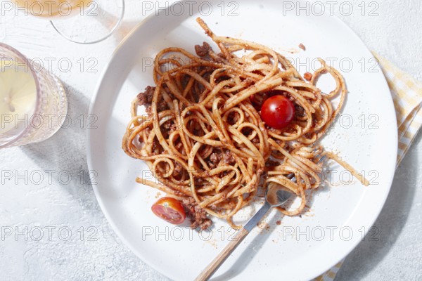 A plate holds freshly cooked spaghetti topped with flavorful meat sauce and garnished with bright cherry tomatoes. A glass sits nearby, reflecting a relaxed dining atmosphere