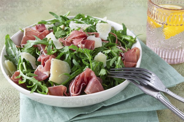 Fresh arugula salad with prosciutto and grated parmesan cheese, on a plate, homemade, no people