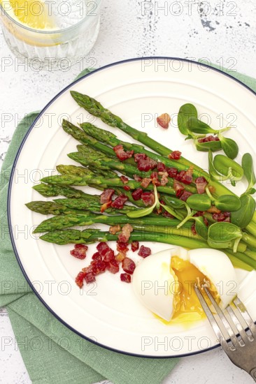 Poached egg with fork, asparagus, bacon slices and herbs, on a white plate, breakfast, close-up, no people