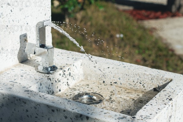 A clean tap fountain dispenses fresh water in a park surrounded by greenery. Sunlight shines on the water, creating a refreshing atmosphere for visitors enjoying the outdoors