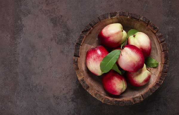Ripe nectarine, in a wooden plate, brown background, top view, no people