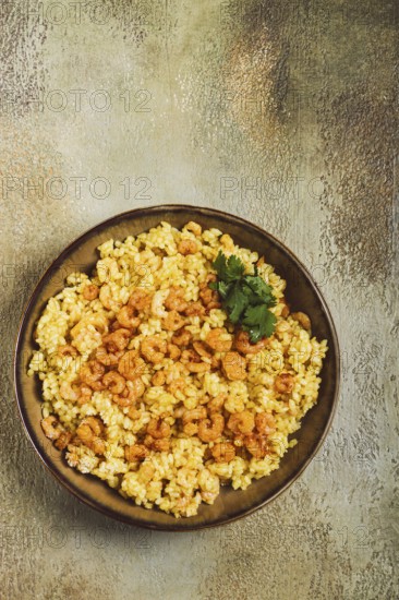 Risotto with shrimp, in a bowl, on a textured surface, with a side dish of fresh coriander, homemade, no people