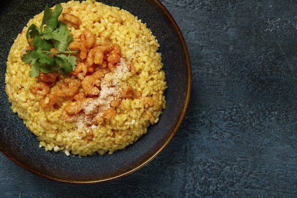 Risotto with shrimp, in a bowl, on a textured surface, with a side dish of fresh coriander, homemade, no people