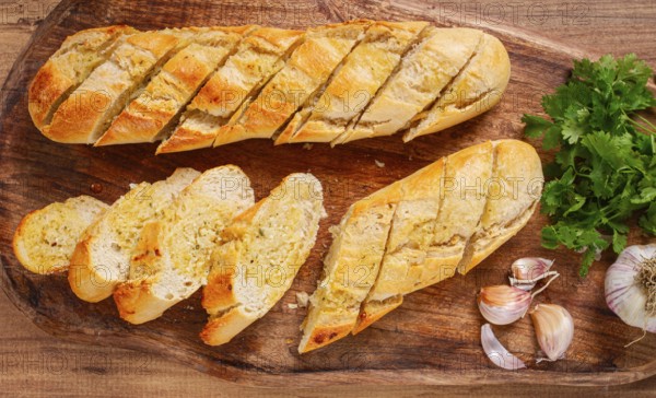 Garlic bread, baguette with garlic butter and herbs, on a wooden board, with herbs and garlic cloves