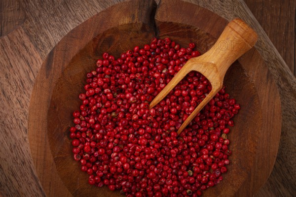Bright red peppercorns, in a wooden bowl, with a small wooden tray