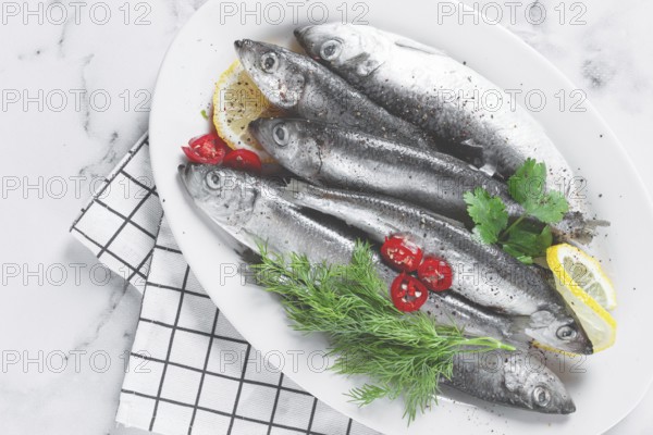 Fresh Herring fish, ready to cook, with herbs and spices, on a white platter, in the kitchen