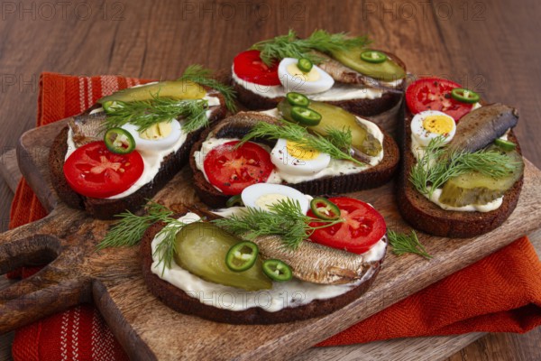 Sandwiches on rye bread with sprats, quail eggs, fresh tomatoes and pickled cucumber, on a wooden board, appetizer, breakfast