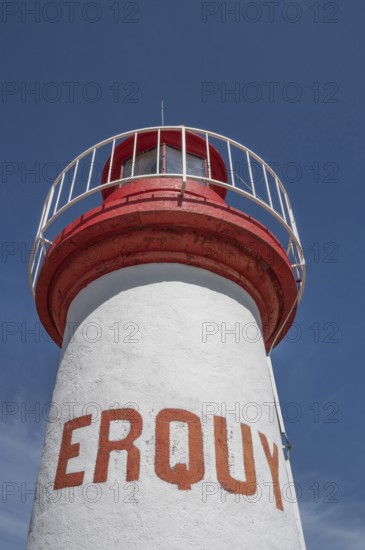 An extreme bottom view shows the upper, cylindrical part of the white-red lighthouse of Erquy, whose name is written in large, orange block letters on the tower shaft, against a bright blue sky, Erquy, Cap d'Erquy, Côtes-d'Armor department, Brittany region, France