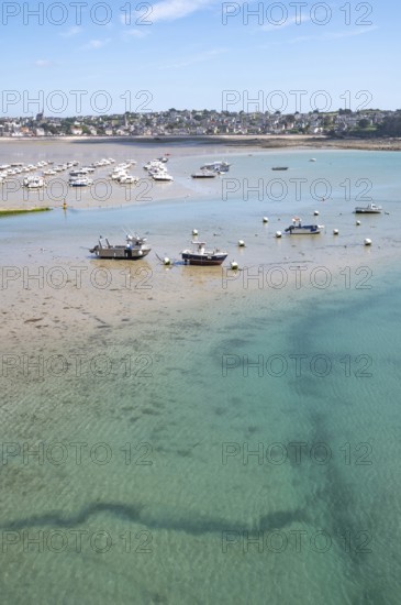 Over the shallow, turquoise water and moist sandy soil at low tide (low tide), with the shadows of currents and rocks visible in the water and numerous small boats dry in the background, Erquy, Saint-Brieuc Bay, Côtes-d'Armor Department, Brittany Region, France