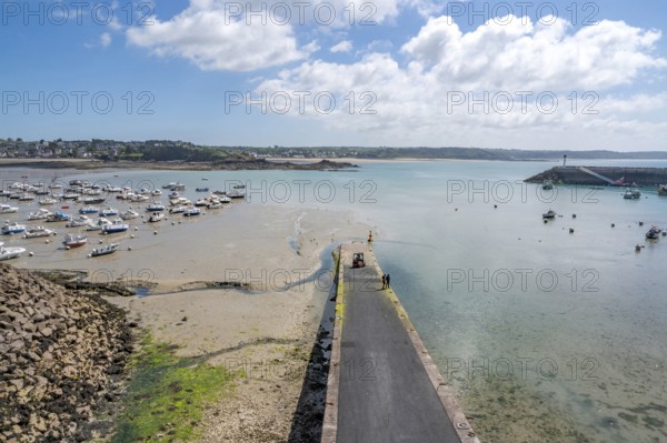 A long, dark pier juts out into the shallow harbor area, where numerous sailing and fishing boats dry on the moist sand at low tide, while in the background you can see the calm sea and a wooded coastline, Erquy, Saint-Brieuc Bay, Côtes-d'Armor, Brittany region, France