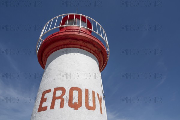 An extreme bottom view shows the upper, cylindrical part of the white-red lighthouse of Erquy, whose name is written in large, orange block letters on the tower shaft, against a bright blue sky, Erquy, Cap d'Erquy, Côtes-d'Armor department, Brittany region, France