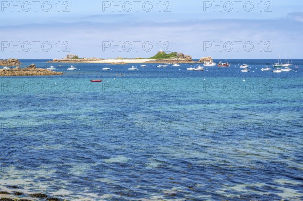 A large rock of pink granite shaped by wind and weather dominates the right foreground, while in the background the bright turquoise-blue water of the Atlantic is crossed by numerous sailboats and the small, island-like headland with the Saint-Gildas lighthouse, Port Blanc, Penvenan, Cotes-d'Armor department, Brittany region, France