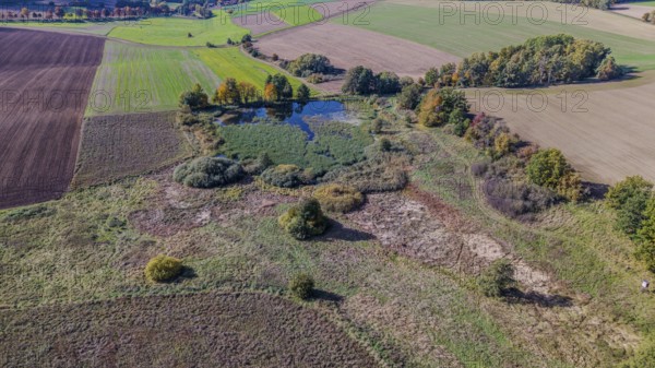 An extensive natural landscape shows a pond surrounded by colorful trees. The fields are green and brown, typical colors of late autumn. Železná hurka, Czech Republic