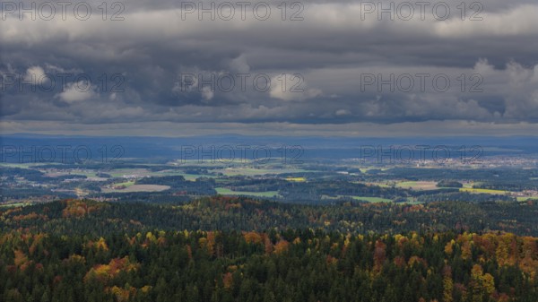 From a viewpoint, you can see a wide valley surrounded by colorful forests. The sky is cloudy and creates an atmospheric atmosphere in autumn. Altglashütte, Upper Palatinate