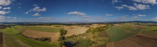 A large, open landscape shows green and brown fields with scattered trees. The sky is clear and sunny, clouds are passing by. Železná hurka, Czech Republic