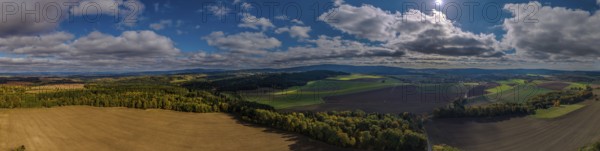 A breathtaking landscape with vast fields and deep blue skies. Sunlight shines onto the green area. Clouds gently pass by. Železná hurka, Czech Republic