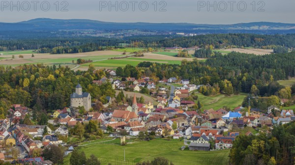 A gentle hilly landscape surrounds a small village with colorful houses and an old castle. The golden autumn colors decorate the landscape and create a peaceful atmosphere. Falkenberg, Upper Palatinate