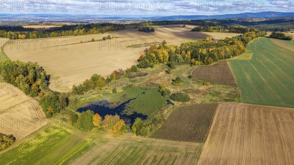 Colourful autumn colors characterize the rural scene with a small pond surrounded by meadows and fields. Nature is in full splendor under blue skies. Železná hurka, Czech Republic