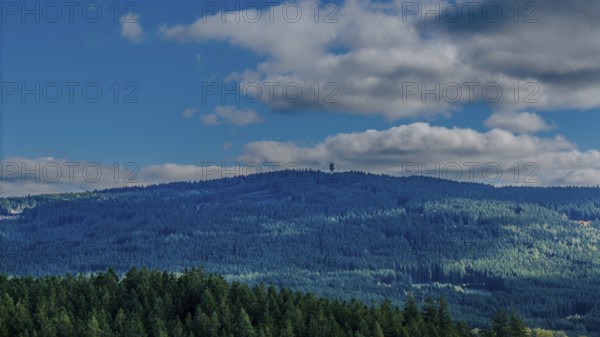 A green, wooded hill in the Bohemian Forest is visible under a blue sky with few clouds. Nature is calm and inviting, ideal for hikers. Dylen, Czech Republic