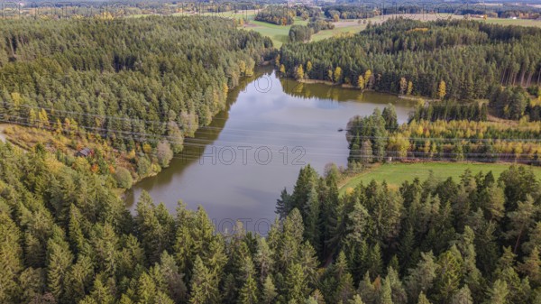 A picturesque forest lake is surrounded by tall, green trees. The autumn colors are reflected in the calm water, while clouds adorn the sky. Falkenberg, Upper Palatinate