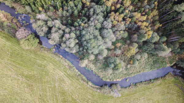 This scene shows a gently flowing river surrounded by colorful trees. The colors of autumn give the landscape a picturesque look. Falkenberg, Upper Palatinate