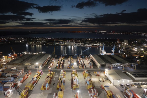 Night view of a bustling port with illuminated containers and cranes by the waterfront. Aerial view to a container unloading terminal of port of Burgas, Bulgaria at night. Logistics and transport