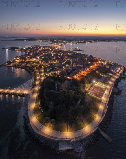 Historic peninsula illuminated at twilight, surrounded by calm sea waters. Aerial view to old town of Nessebar, Bulgaria night time