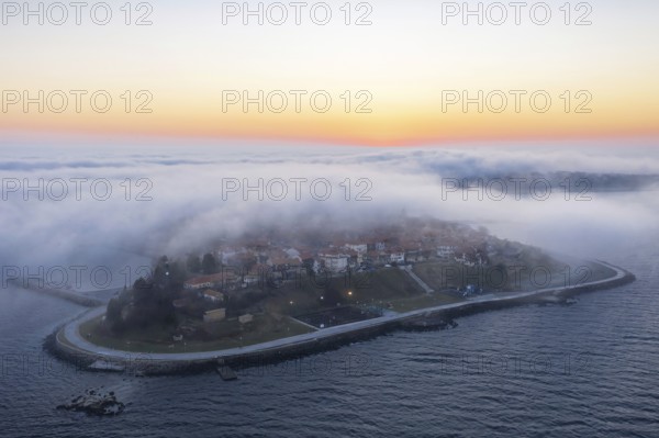 An island surrounded by mist at sunrise with calm waters. Aerial view to thick fog descends over the Nessebar, Burgas, Bulgaria