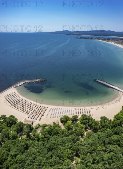 Scenic beach with lined umbrellas beside lush greenery and an expansive ocean. Aerial view to beautiful Perla beach near to Primorsko, Bulgaria