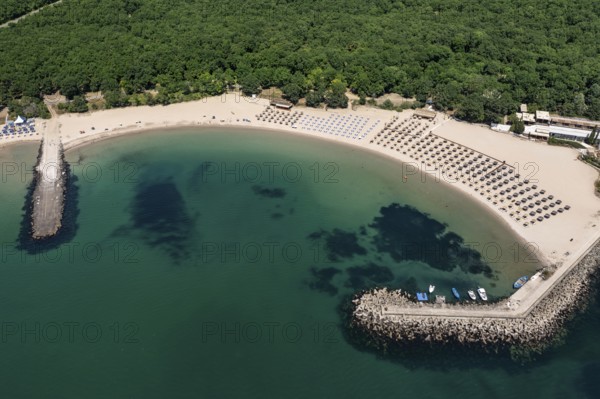 Beach lined with umbrellas and adjacent to lush greenery beside calm waters. Aerial view to beautiful Perla beach near to Primorsko, Bulgaria