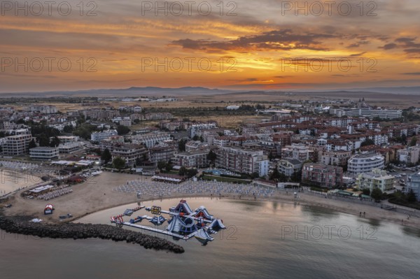 Aerial view of a coastal city at sunset with a calm sea, sandy beach, and vibrant sky. Aerial view to a sea resort Ravda, Bulgaria and beautiful sunset
