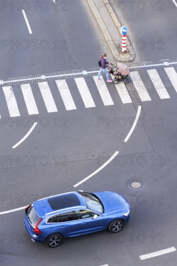 Blue car heading to pedestrian crossing with unrecognizable young woman pushing baby carriage, safety of self-driving autonomous technology concept, aerial birds eye view Prague Czech republic