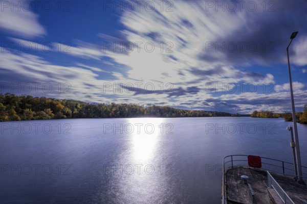 A quiet river stretches under a cloudy sky. The clouds move gently while the sunlight makes the water surface sparkle. Landau an der Isar, Lower Bavaria
