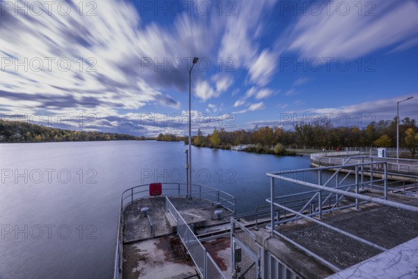 A beautiful view of a peaceful river in cloudy weather. Trees on the shore show autumnal colors, while clouds pass by quickly. Landau an der Isar, Lower Bavaria