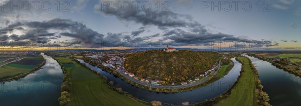 The Bogenberg with the pilgrimage church of the Assumption of the Virgin rises above the quiet Danube. The surrounding area shows green fields and the clouds reflect the light of the setting sun. Bogen, Lower Bavaria