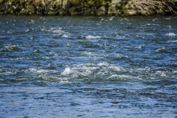 The clear water surface of a river shows soft waves that are created by the movement of the water. The surrounding area looks peaceful and natural. Landau an der Isar, Lower Bavaria