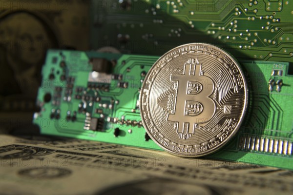 Silver bitcoin coin with dollars and computer motherboard, cryptocurrency mining and investing concept Prague Czech republic