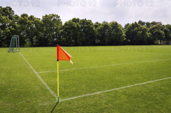 Orange vivid corner flag on fresh green football ground, trees in background, sunny summer day Prague Czech republic