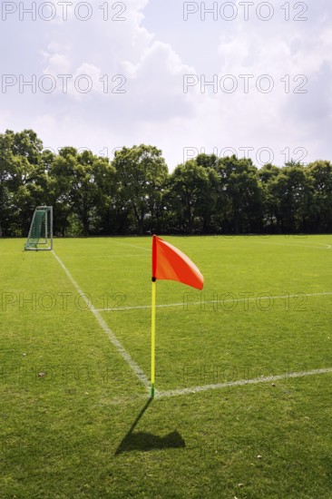 Orange vivid corner flag on fresh green football ground, trees in background, sunny summer day Prague Czech republic