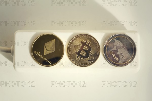 Bitcoin, Ethereum and Ripple coins lying on power strip extension cord with 3 sockets, largest cryptocurrencies by market capitalization, cryptocurrency investing, energy consumption and footprint concept Prague Czech republic