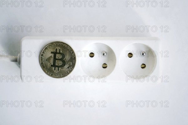 Bitcoin coin lying on power strip extension cord with two empty sockets, cryptocurrency investing, energy consumption and footprint concept, isolated on white background Prague Czech republic