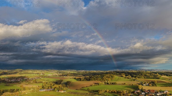 A rainbow stretches across the vast fields and villages. The scene shows vivid colors under a cloudy sky in autumn. It is quiet and peaceful. Bogen, Lower Bavaria