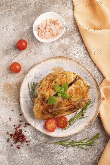 Fried Turkey Thigh with spices and rosemary on plate on brown concrete background and orange linen textile. top view, flat lay, close up