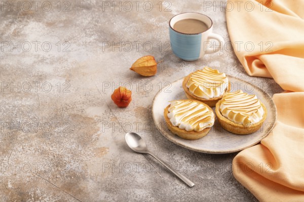 French lemon tart with meringue on brown concrete background, cup of coffee, orange linen textile, side view, copy space