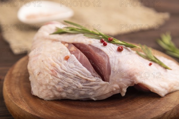 Raw Turkey Thigh with spices and rosemary on cutting board on brown wooden background and linen textile. side view, close up, selective focus
