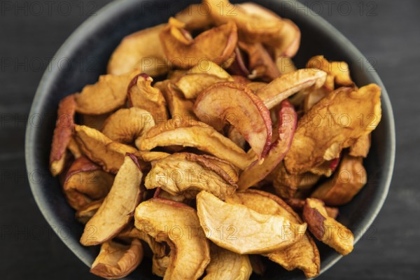 Dried Apples in ceramic bowl on black wooden background. Side view, close up. healthy food, minimalism. sweet, selective focus
