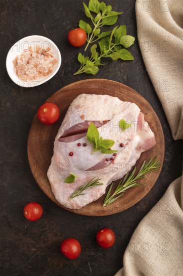 Raw Turkey Thigh with spices and rosemary on cutting board on black concrete background and linen textile. top view, flat lay, close up