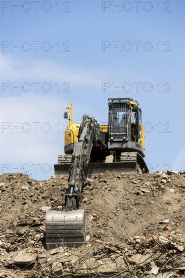 Yellow construction digger, excavator on demolition site stand on debris, sunny day clear blue sky, Prague, Czech republi